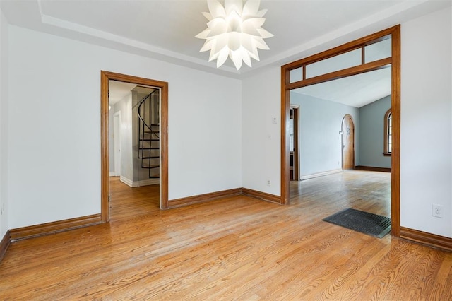 empty room featuring light hardwood / wood-style floors, a tray ceiling, and an inviting chandelier