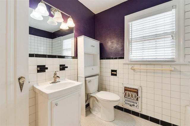 bathroom with tile patterned floors, heating unit, toilet, vanity, and tile walls