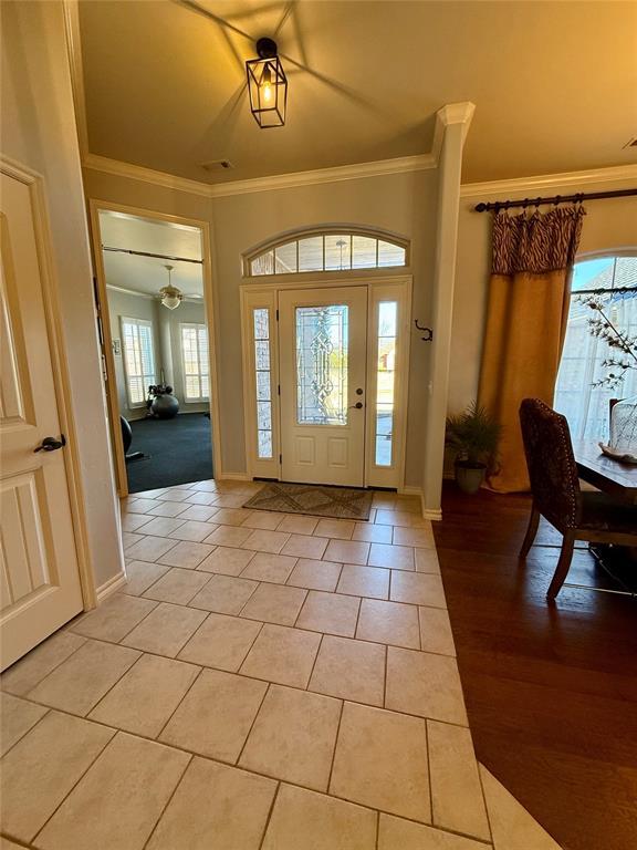 entryway with light tile patterned floors and ornamental molding