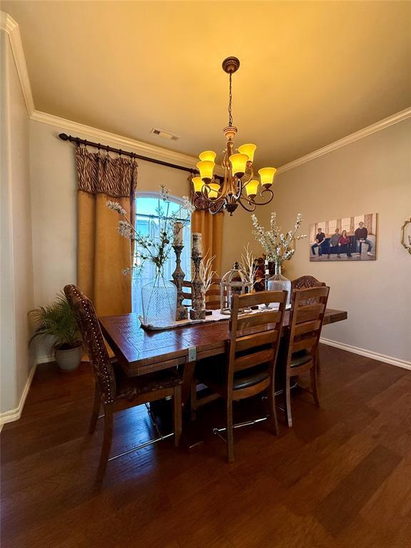 dining space featuring dark hardwood / wood-style flooring, ornamental molding, and an inviting chandelier