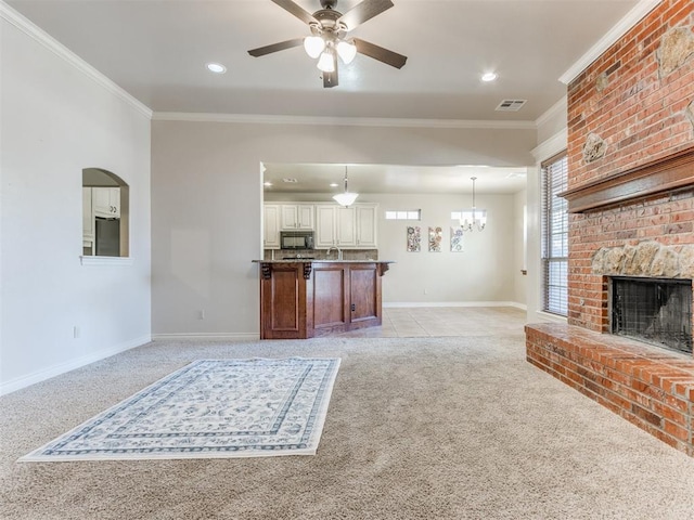 carpeted living room with ornamental molding, a brick fireplace, sink, and ceiling fan with notable chandelier