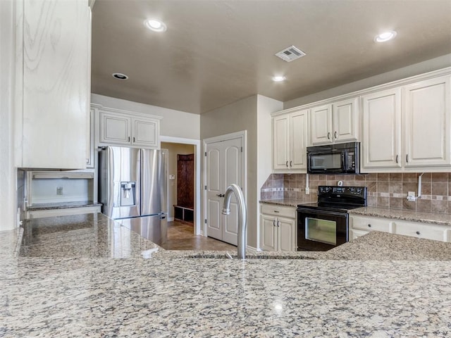 kitchen with sink, light stone countertops, black appliances, white cabinets, and decorative backsplash