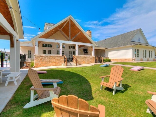 back of property featuring a patio area, a chimney, outdoor dry bar, and a lawn