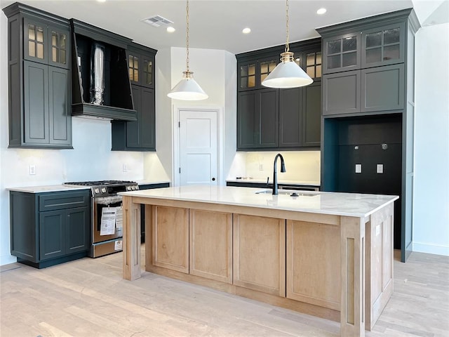 kitchen with stainless steel gas range oven, a sink, visible vents, ventilation hood, and a center island with sink