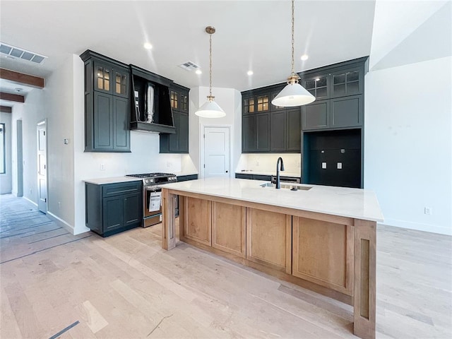 kitchen featuring visible vents, wall chimney exhaust hood, light wood-style flooring, stainless steel range with gas stovetop, and a sink