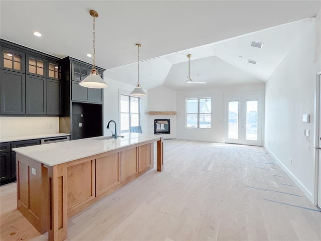 kitchen featuring light wood-style flooring, a sink, vaulted ceiling, light countertops, and an island with sink