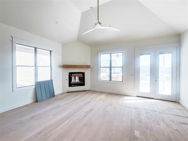 unfurnished living room featuring ceiling fan, light wood-style flooring, vaulted ceiling, french doors, and a glass covered fireplace