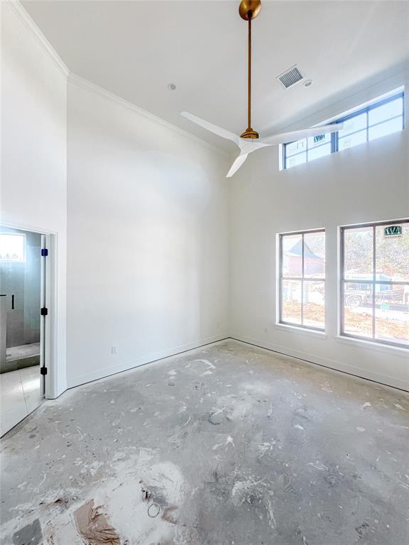 empty room with baseboards, a high ceiling, visible vents, and crown molding