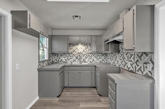 kitchen with tile countertops, sink, gray cabinetry, and a textured ceiling