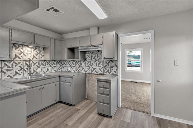 kitchen featuring backsplash, sink, gray cabinets, a textured ceiling, and tile counters