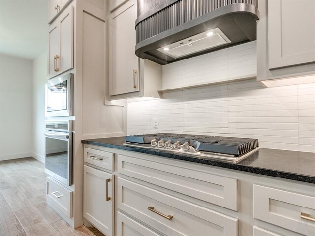 1203 Jaden Blvd, Tuttle, OK 73089 - kitchen featuring appliances with stainless steel finishes, wall chimney exhaust hood, tasteful backsplash, and light wood-style flooring