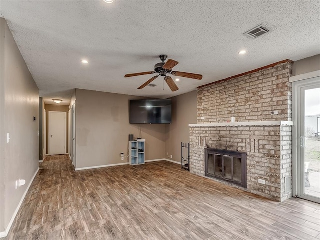 unfurnished living room with hardwood / wood-style flooring, ceiling fan, a brick fireplace, and a textured ceiling