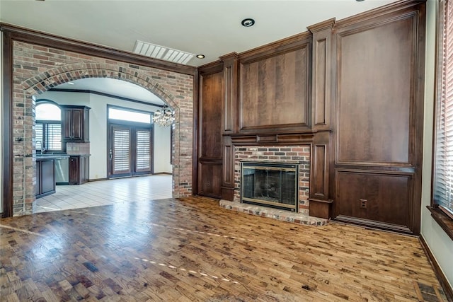 unfurnished living room featuring crown molding, light hardwood / wood-style floors, brick wall, and a brick fireplace