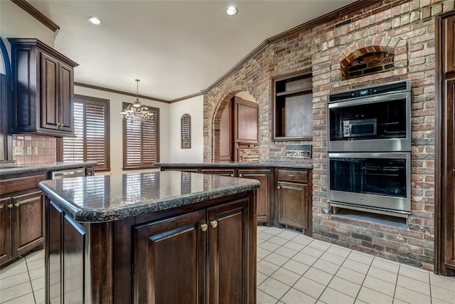 kitchen featuring backsplash, stainless steel double oven, a notable chandelier, a kitchen island, and dark brown cabinets