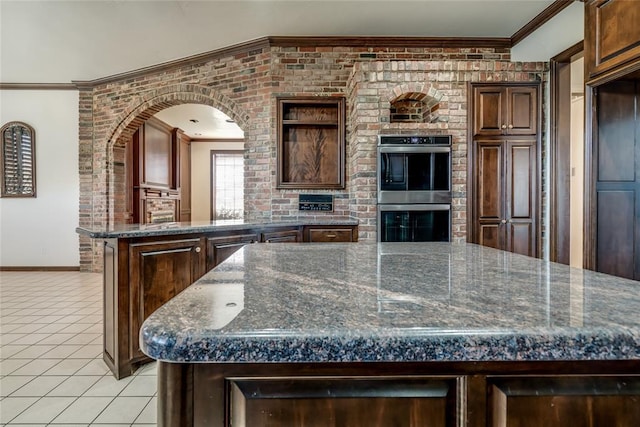 kitchen featuring light tile patterned flooring, crown molding, a kitchen island, stainless steel double oven, and brick wall