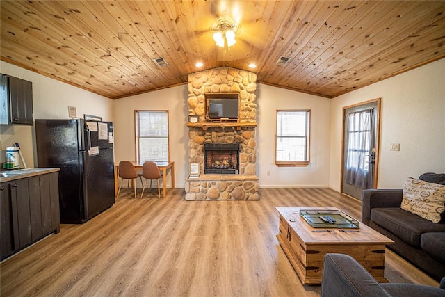 living room featuring lofted ceiling, light hardwood / wood-style floors, a stone fireplace, and wooden ceiling