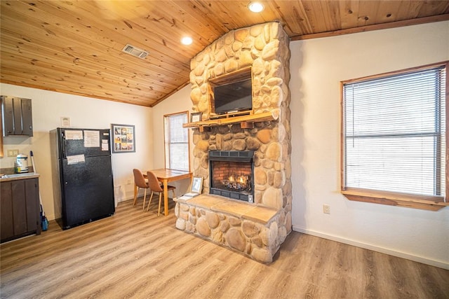 living room featuring light hardwood / wood-style floors, vaulted ceiling, a stone fireplace, and wood ceiling