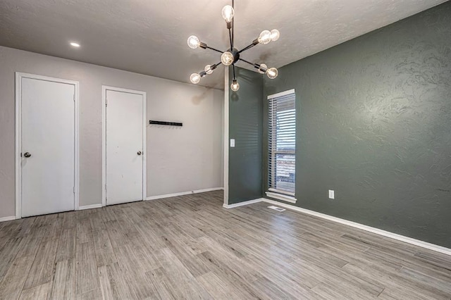 unfurnished bedroom with a notable chandelier, light wood-type flooring, a textured ceiling, and multiple closets