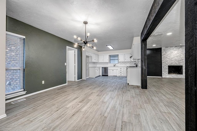 kitchen with dishwasher, white cabinets, a stone fireplace, light wood-type flooring, and a notable chandelier