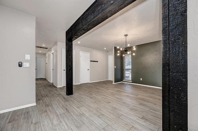 empty room with light hardwood / wood-style floors and an inviting chandelier