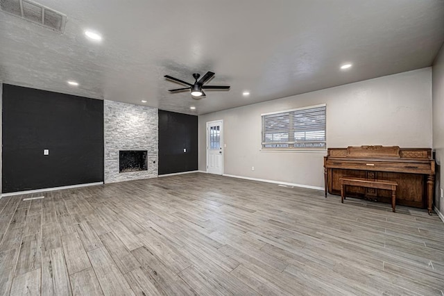 unfurnished living room with light hardwood / wood-style floors, a stone fireplace, and ceiling fan