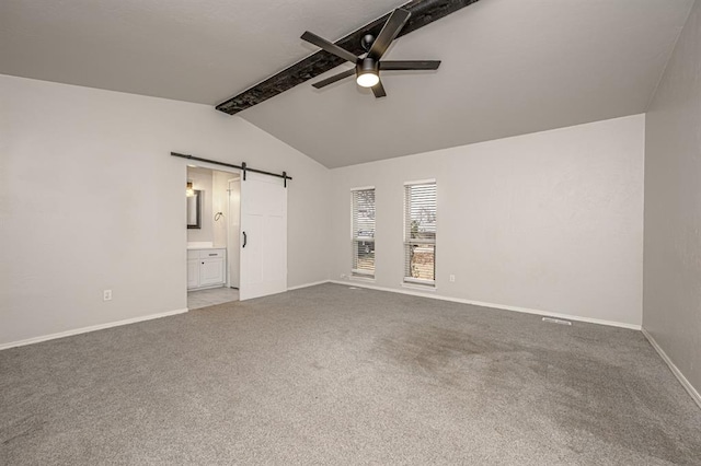 unfurnished bedroom featuring ensuite bath, ceiling fan, a barn door, lofted ceiling with beams, and carpet floors