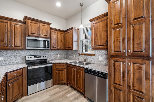 kitchen with appliances with stainless steel finishes, light stone counters, sink, light hardwood / wood-style floors, and hanging light fixtures