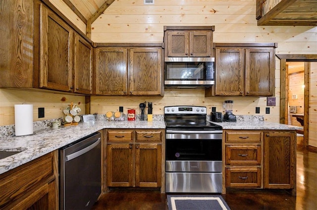 kitchen with lofted ceiling, wooden walls, stainless steel appliances, and light stone counters