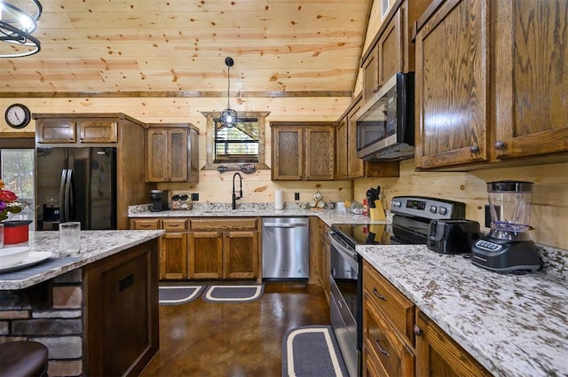 kitchen featuring light stone countertops, stainless steel appliances, sink, hanging light fixtures, and wood walls