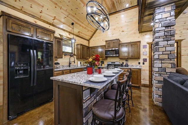 kitchen with a center island, hanging light fixtures, wooden walls, appliances with stainless steel finishes, and decorative columns