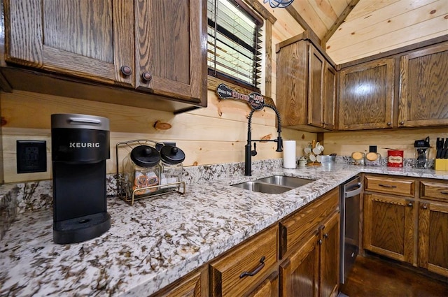 kitchen with sink, light stone counters, stainless steel dishwasher, wood walls, and lofted ceiling