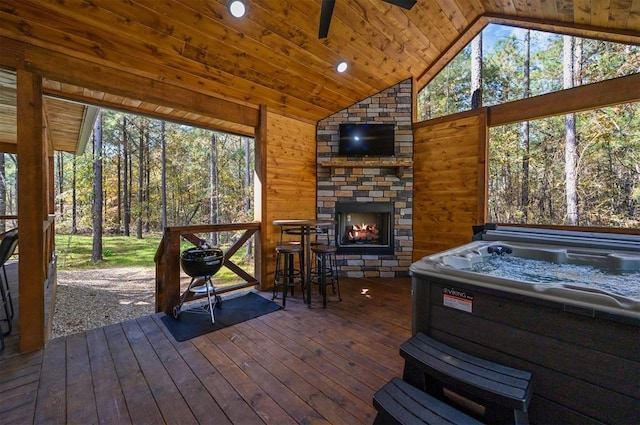 sunroom with ceiling fan, a hot tub, an outdoor stone fireplace, lofted ceiling, and wood ceiling