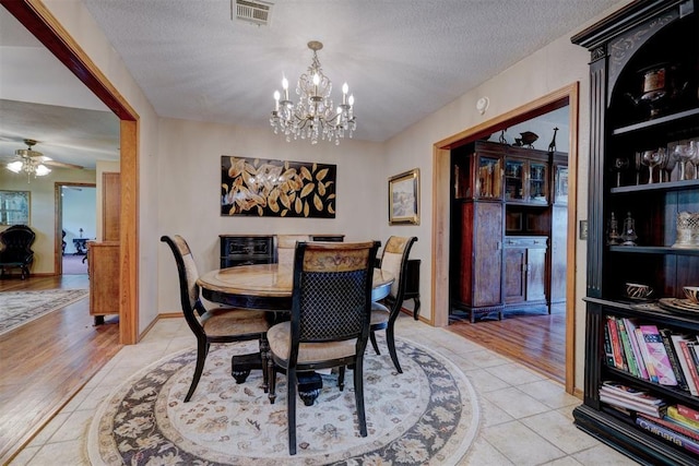 tiled dining area featuring ceiling fan with notable chandelier and a textured ceiling