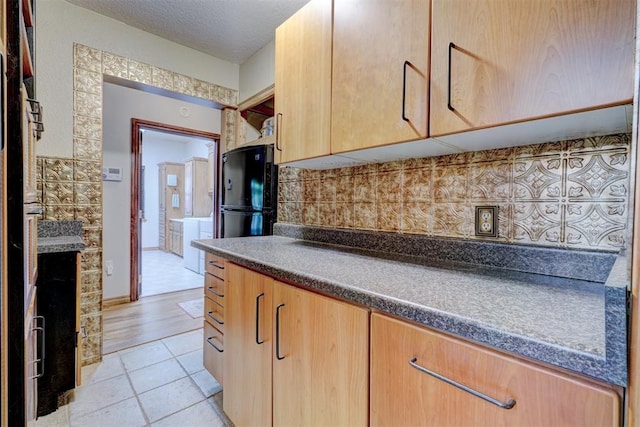 kitchen with black fridge, decorative backsplash, light tile patterned floors, light brown cabinetry, and washer / clothes dryer