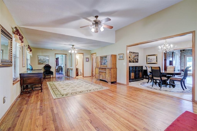 living room with ceiling fan with notable chandelier, light hardwood / wood-style flooring, and lofted ceiling