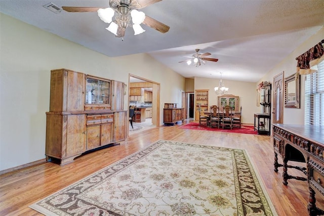 living room with ceiling fan with notable chandelier, light wood-type flooring, a textured ceiling, and vaulted ceiling