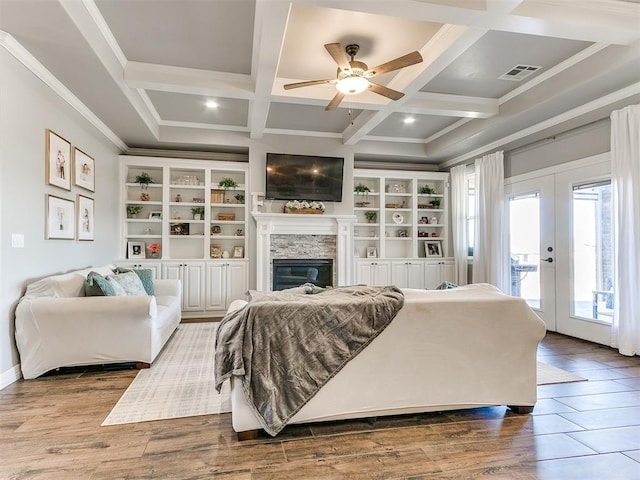 living room with coffered ceiling, french doors, a stone fireplace, built in shelves, and wood-type flooring