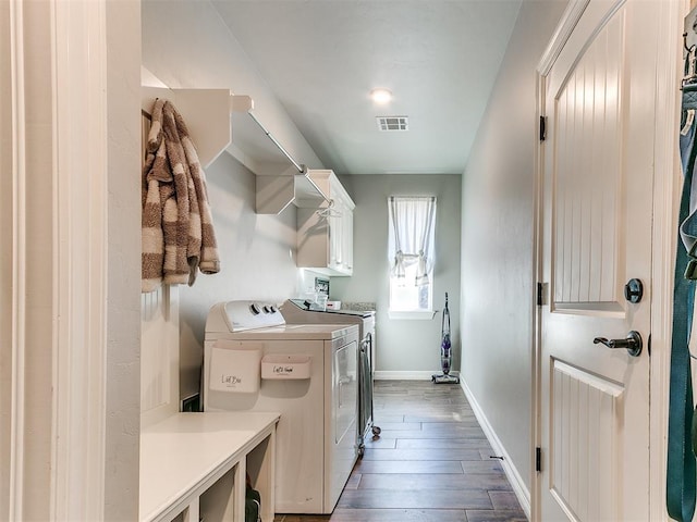 clothes washing area with washing machine and dryer, dark wood-type flooring, and cabinets