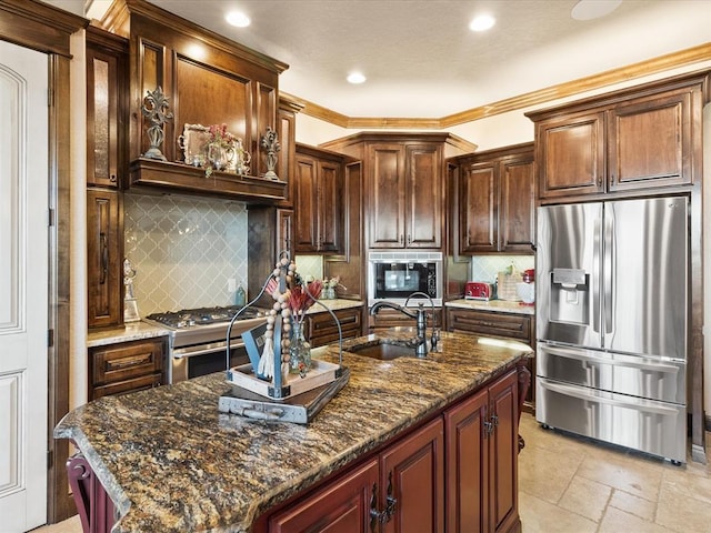 kitchen with appliances with stainless steel finishes, sink, dark stone countertops, and a kitchen island with sink