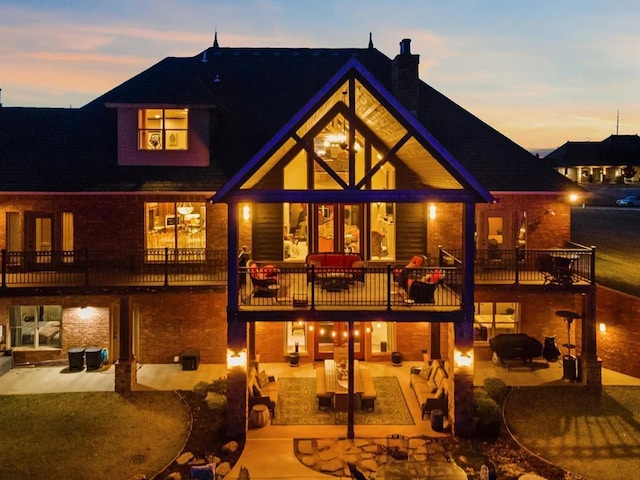 5451 Cottonwood Creek Cir, Norman, OK 73069 - back of property at dusk with a balcony, a chimney, a patio, and brick siding