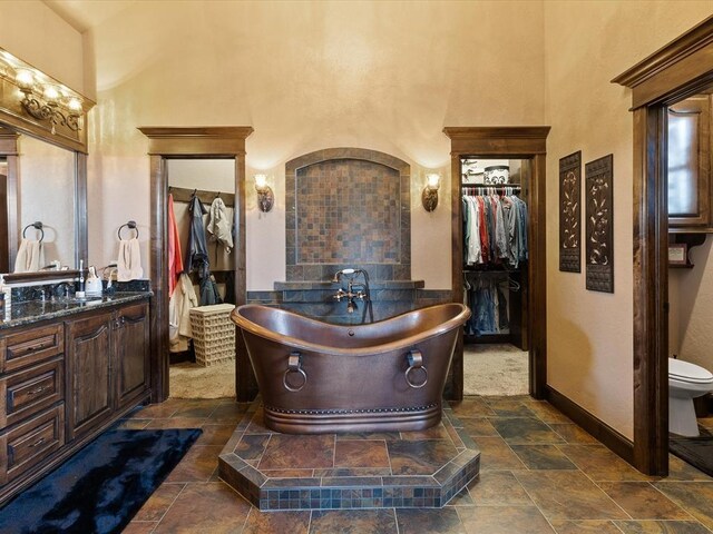 5451 Cottonwood Creek Cir, Norman, OK 73069 - bathroom with vanity, a walk in closet, a high ceiling, a soaking tub, and stone tile flooring