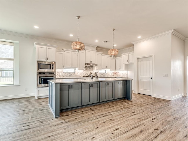 kitchen with white cabinetry, hanging light fixtures, light hardwood / wood-style flooring, a kitchen island with sink, and appliances with stainless steel finishes