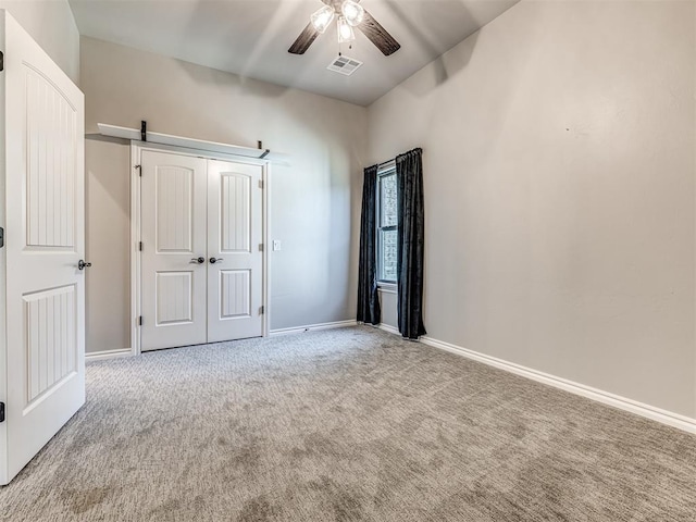 unfurnished bedroom featuring ceiling fan, a barn door, and carpet floors