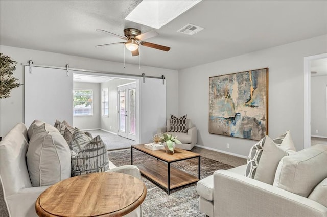 carpeted living room with a barn door, a skylight, and ceiling fan