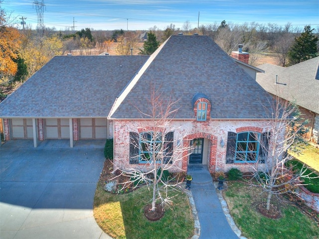 view of front of property with a shingled roof, concrete driveway, brick siding, and a chimney