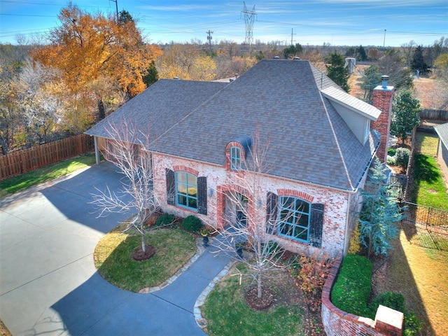 view of front of home with fence, driveway, roof with shingles, a front lawn, and a chimney