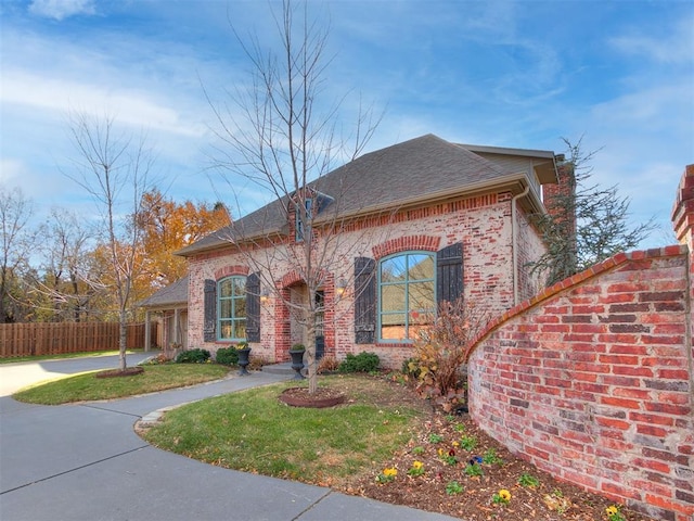 french provincial home with brick siding, roof with shingles, and fence