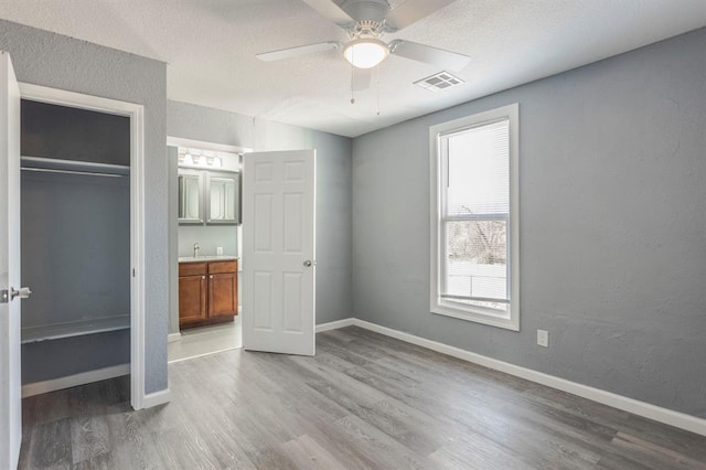 unfurnished bedroom with sink, ceiling fan, a textured ceiling, a closet, and light wood-type flooring