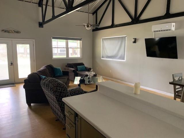 living room with french doors, ceiling fan, high vaulted ceiling, an AC wall unit, and light hardwood / wood-style floors