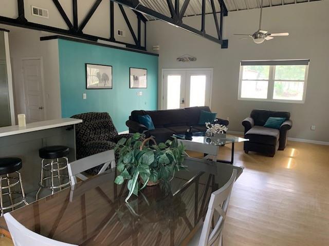 dining space featuring french doors, light wood-type flooring, ceiling fan, and a high ceiling